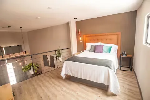 Recámara en mezzanine del Loft de diseño Suites 509, Pachuca: cama queen, cabecera capitoné y barandal industrial