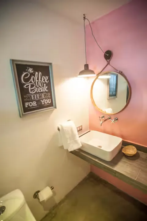 Baño del Loft de diseño Suites 509, Pachuca: lavabo sobre encimera, pared salmón, espejo redondo y estilo boutique