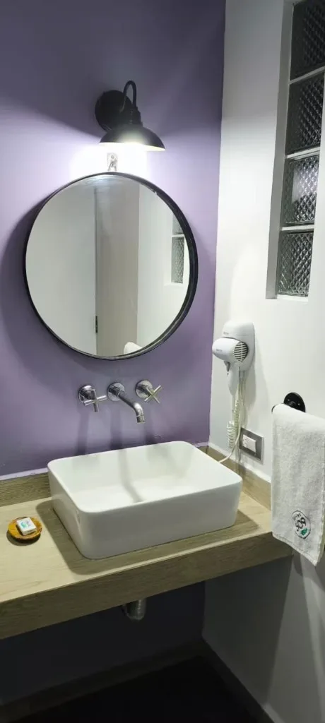 Lavabo del baño en Suites 509, Pachuca: espejo redondo, pared morada, secador y toallas Suites 509