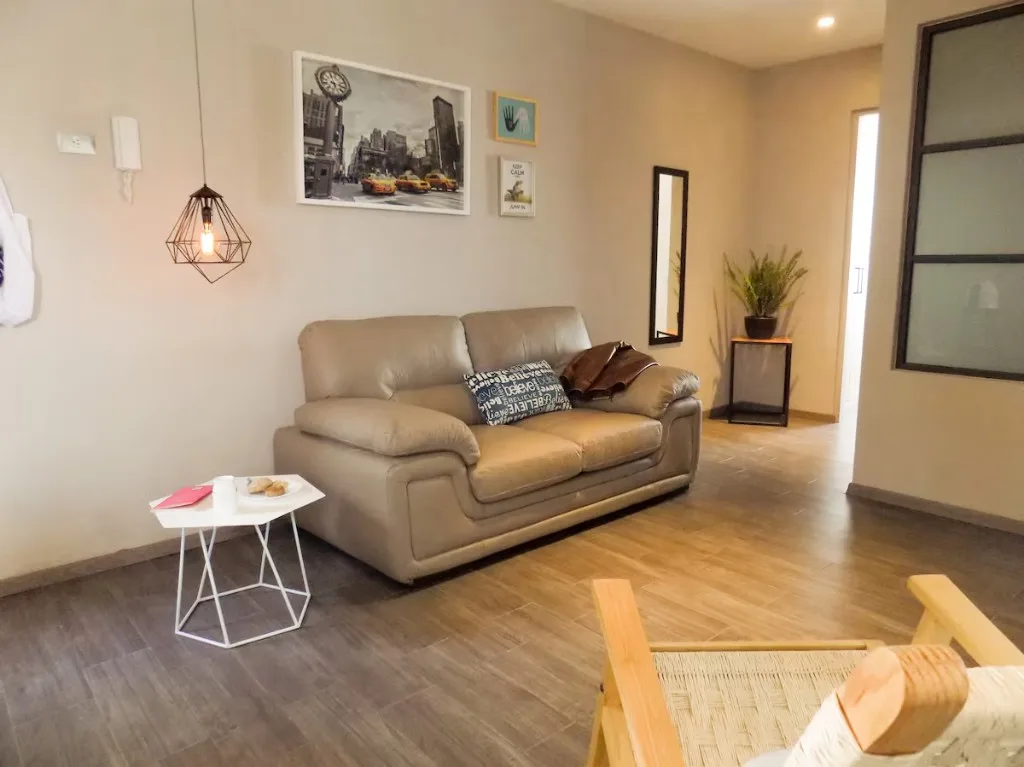 Sala de estar en Suite Terraza Suites 509, Pachuca: sofá color arena, lámpara industrial, arte urbano y mesa de centro — ambiente acogedor