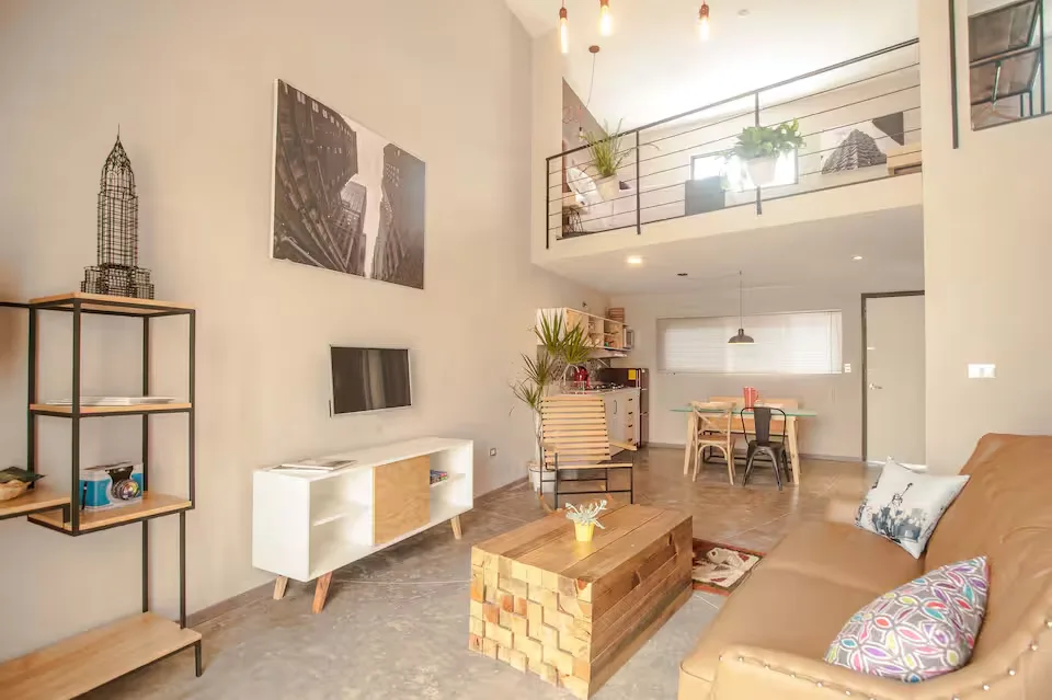 Sala de loft de diseño Suites 509, Pachuca: sofá de piel, TV, mezanine con barandal de metal y piso de concreto pulido